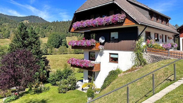 Una cabaña tradicional con balcones, rodeada de exuberante vegetación y montañas.