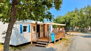 Una casa móvil con porche, una pequeña terraza y un letrero azul.