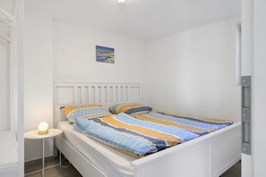 Un lit simple avec une couverture à rayures, une table de chevet avec une lampe et un petit tableau accroché au mur.