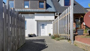 A pathway leading to a house with a white door, a wooden fence, and a brick wall.