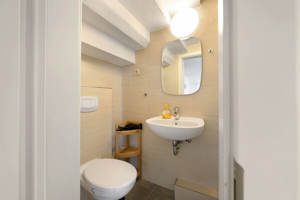 A small bathroom with a toilet, a sink, a mirror, and a shelf.