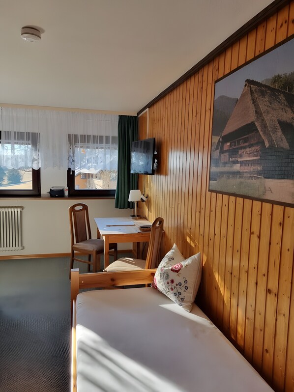 Une piĂšce comprenant un lit, un bureau, une chaise, un tĂ©lĂ©viseur et une fenĂȘtre avec des rideaux.