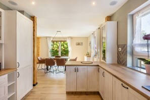 Een moderne keuken met houten kastjes, een eethoek met stoelen, en een raam met uitzicht op groen.