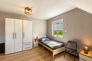 Un dormitorio con cama, armario, silla, mesita de noche, l ámpara y ventana.