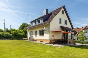 Een huis met twee verdiepingen, een schuin dak, een overdekt terras en een verzorgd gazon.