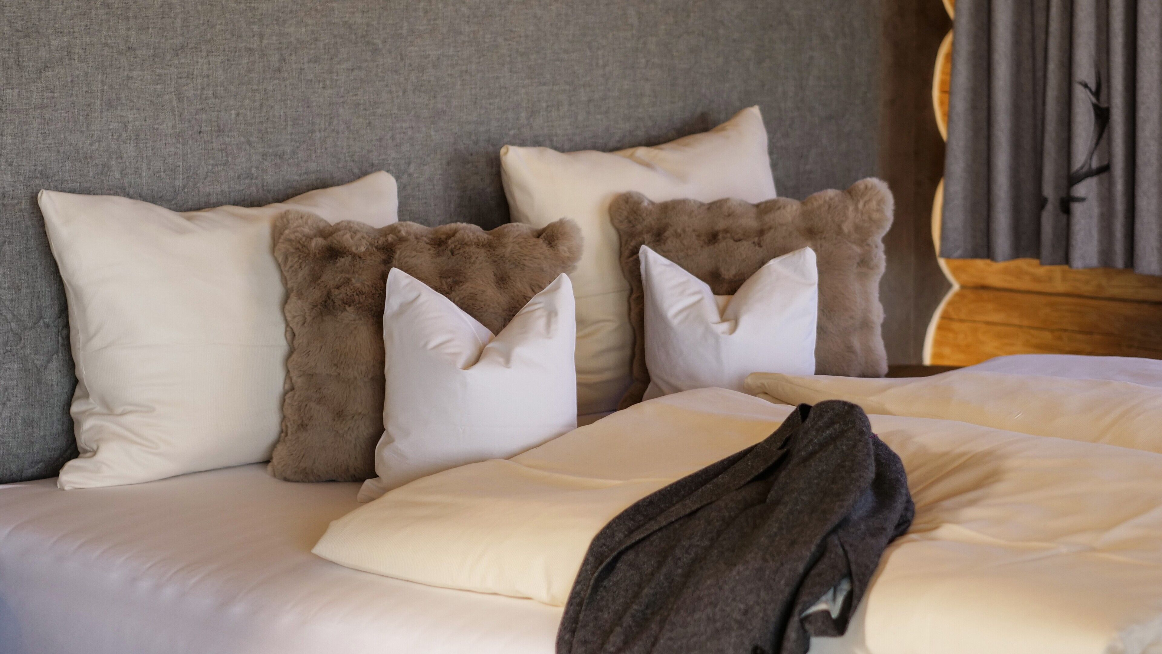 A bed with white and brown pillows, a grey headboard, and a wooden headboard on the right.