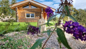 A log cabin with a window, surrounded by a garden with various plants and flowers.