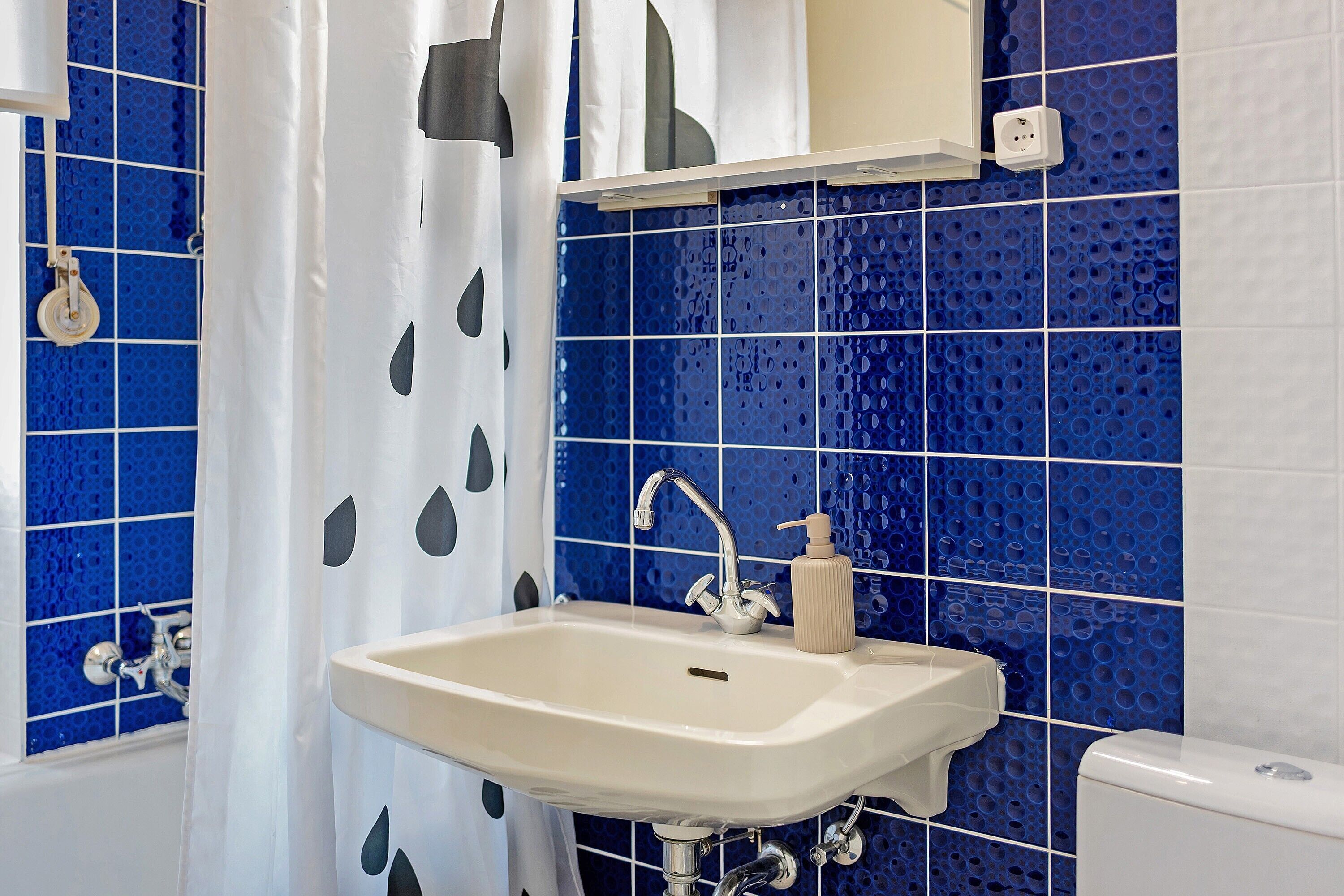 A bathroom with a white sink, a mirror, and a blue tiled wall.