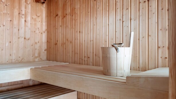 A wooden cabin interior with a bench and a wooden bucket. - Apartment Schanzenblick with Sauna & Pool in the Black Forest (Schönwald im Schwarzwald)