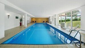 A large indoor swimming pool with clear glass walls, a tiled floor, and a few lounge chairs. - Apartment Schanzenblick with Sauna & Pool in the Black Forest (Schönwald im Schwarzwald)