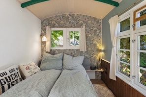 A bedroom with a floral wallpaper, a bed with patterned bedding, a window with curtains, and a nightstand with a lamp. - Tiny Home 'Alma' with Private Garden and Wi-Fi (Fitzen)