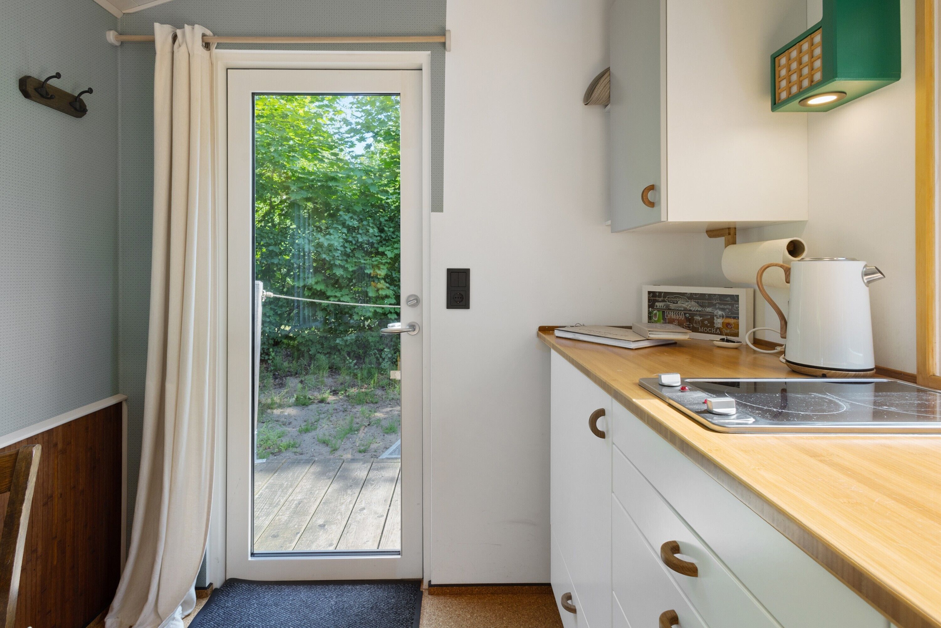 A compact kitchen with a wooden countertop, a kettle, and a view of greenery outside.