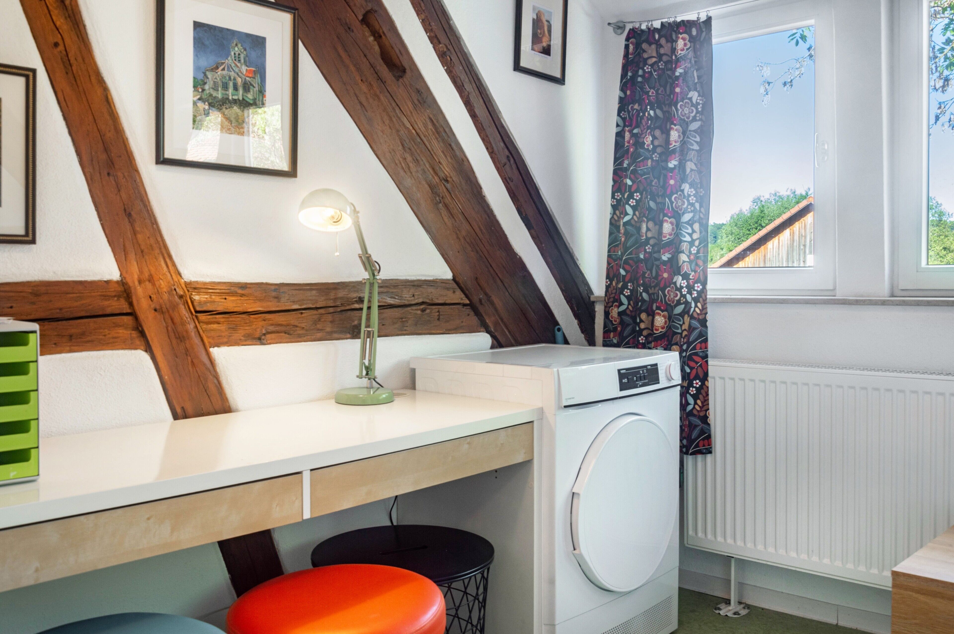 Un espace buanderie comprenant un lave-linge, une table avec une lampe et une fenêtre avec des rideaux.