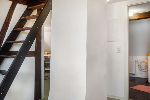 A staircase leading to a room with a white wall, a door, and a visible radiator in the adjacent room.