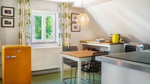 Eine kleine Küche mit Kühlschrank, Mikrowelle, Esstisch mit Stühlen und einem Fenster mit Vorhängen.