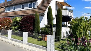 Une maison à deux étages avec un toit en pente, un balcon orné de plantes en pot et une clôture blanche.