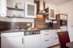 Une cuisine moderne avec des meubles blancs, un évier en acier inoxydable et un four encastré.