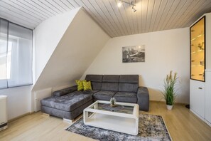 Un salon moderne avec un canapé d’angle, une table basse et un tableau représentant un paysage urbain accroché au mur.