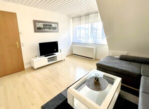 A modern living room with a flat-screen TV, a sofa, a coffee table with a decorative item, a small plant, and a radiator.