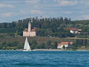 Un paysage côtier avec un voilier, un grand bâtiment doté d’une tour et des vignobles.