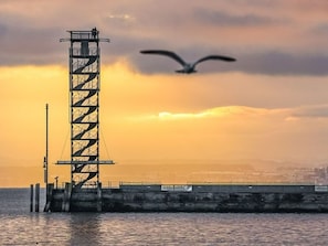 Une haute structure métallique au bord de l’eau, au coucher du soleil.