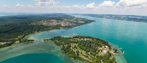 An aerial view of a coastal area with a small island featuring dense greenery and a few buildings.