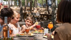 A group of people dining outdoors at a wooden table with various dishes and drinks.