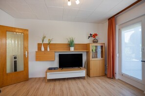 Een moderne woonkamer met een flatscreen televisie, houten kasten en een schuifdeur van glas.