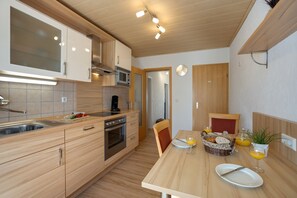 Une cuisine moderne avec des meubles en bois, un four encastré et un coin repas où la table est mise pour le petit-déjeuner.