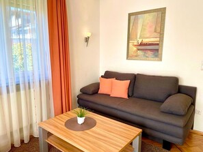 Ein Wohnzimmer mit einer Couch, einem Couchtisch, einem Gemälde und einem Fenster mit Vorhängen.
