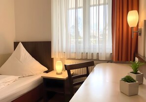Une chambre d’hôtel comprenant un lit, une table de chevet avec une lampe, une chaise, une table et une plante en pot.