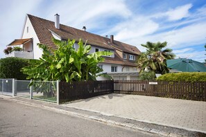 A residential property with a paved driveway, a wooden fence, and a sign indicating a parking area.