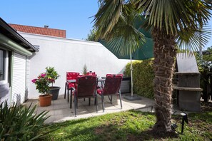 Een terras met een tafel, stoelen, een bloempot en een palmboom.