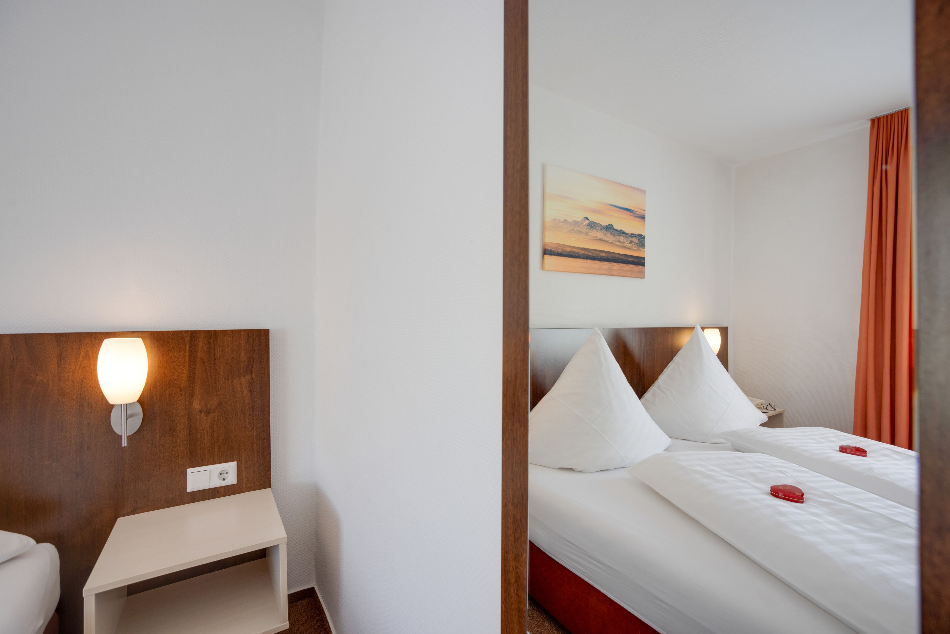 Ein Hotelzimmer mit Bett, Nachttisch, Lampe und einem Gemälde an der Wand.