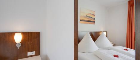A hotel room with a bed, bedside table, lamp, and a painting on the wall.