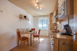 Een kleine keuken met houten kastjes, een eettafel met stoelen en een inbouwmagnetron.