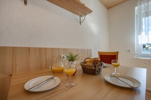 Ein Frühstückstisch mit Tellern, Besteck, einer Glasflasche, einem Glas, einem Korb mit Brot und einem Glas Orangensaft.