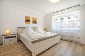 Un dormitorio con una cama, mesitas de noche, persianas en la ventana y dos cuadros colgados en la pared.