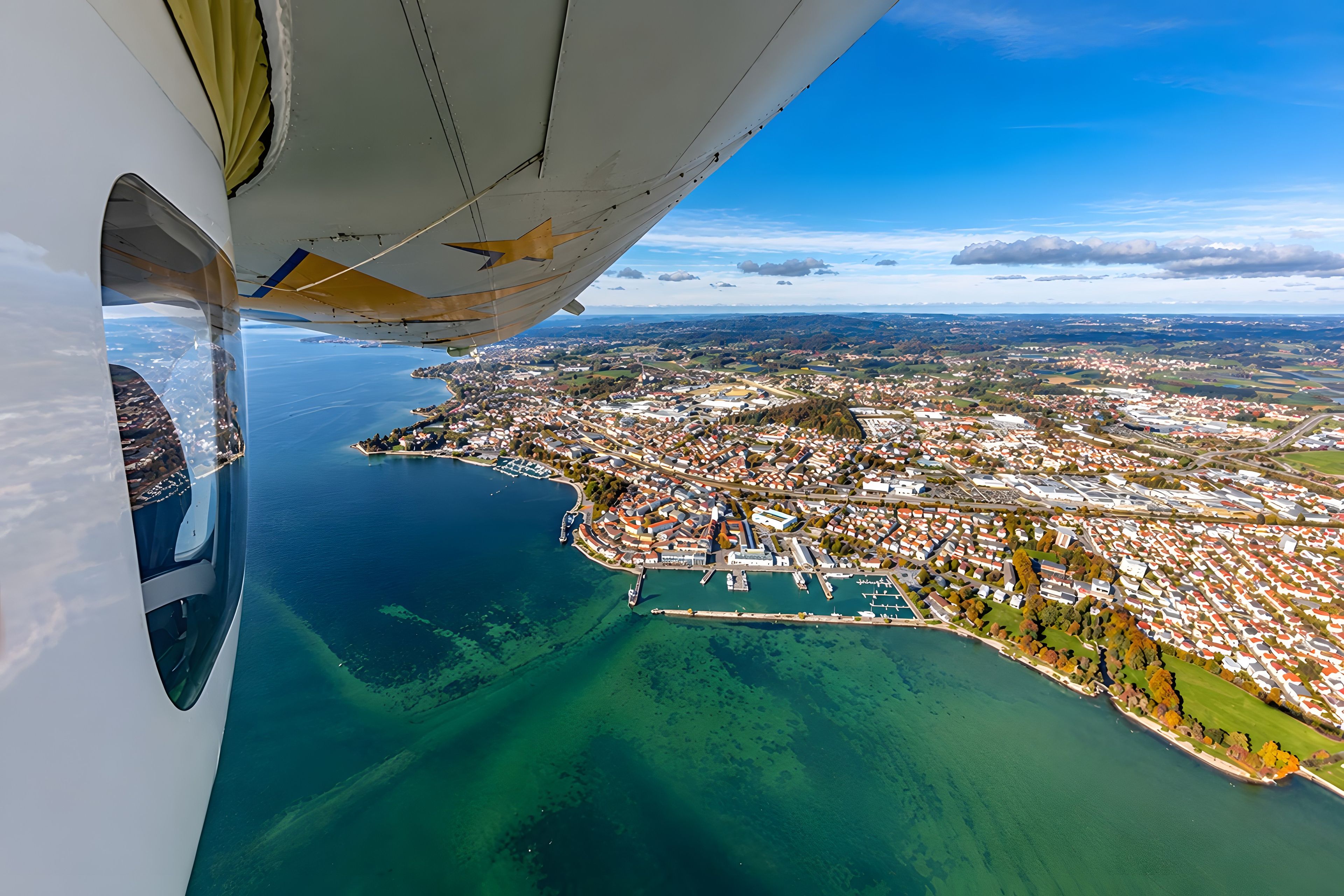 An aerial view of a coastal city with a marina, clear blue waters, and a mix of residential and commercial buildings.