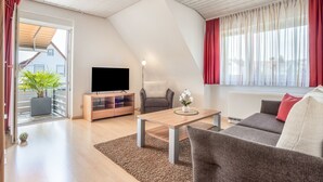 Una sala moderna con un televisor de pantalla plana, una mesa de centro de madera, un sofá gris y una planta en maceta.
