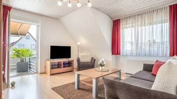 A modern living room with a flat-screen TV, a wooden coffee table, a grey sofa, and a potted plant.