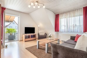 Een moderne woonkamer met een flatscreen televisie, een houten salontafel, een grijze bank en een potplant.