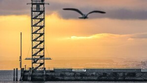 A tall, metal structure by the water during sunset.