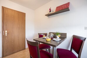 Een eetgedeelte met een houten tafel, rode fauteuils en een klein plankje erboven.