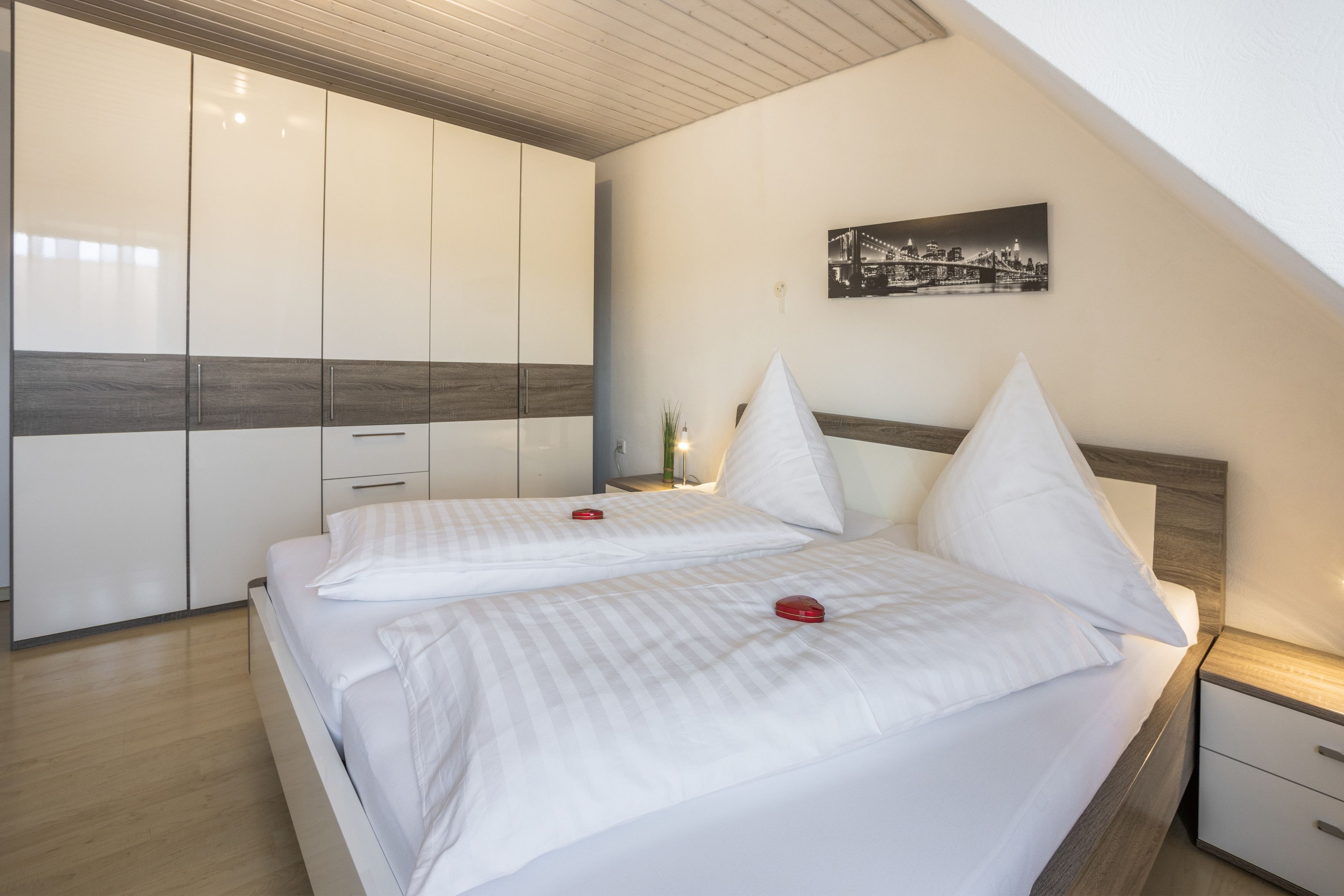 A bedroom with a bed, bedside tables, a nightstand, and a cityscape painting on the wall.