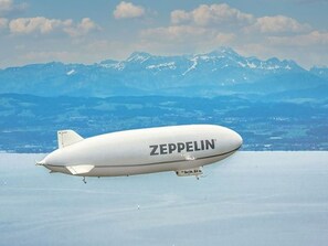 A Zeppelin airship with 'ZEPPELIN' written on its side, flying over a snowy landscape with mountains in the background.