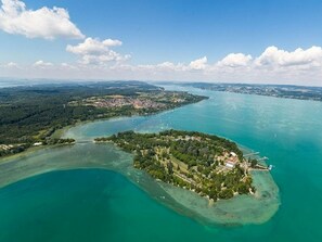 An aerial view of a coastal area with a small island featuring dense greenery and a few buildings. - Apartment 'Zeppelin N T' with Terrace and Wi-Fi (Friedrichshafen)