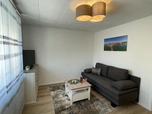 Un salón con un sofá, una mesita con bebidas, un televisor y un cuadro en la pared.