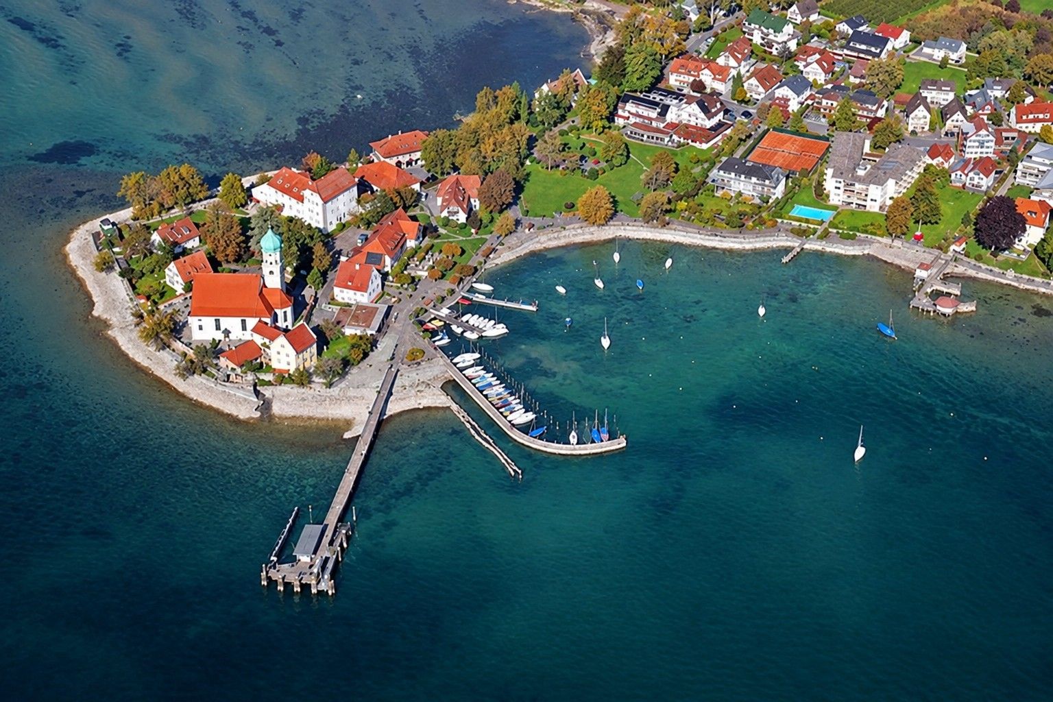 Vue aérienne d’une ville côtière avec un port de plaisance, des maisons et une jetée.