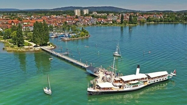 A river with a dock, a large boat, and a small island with buildings. - Apartment 'Zeppelin N T' with Terrace and Wi-Fi (Friedrichshafen)